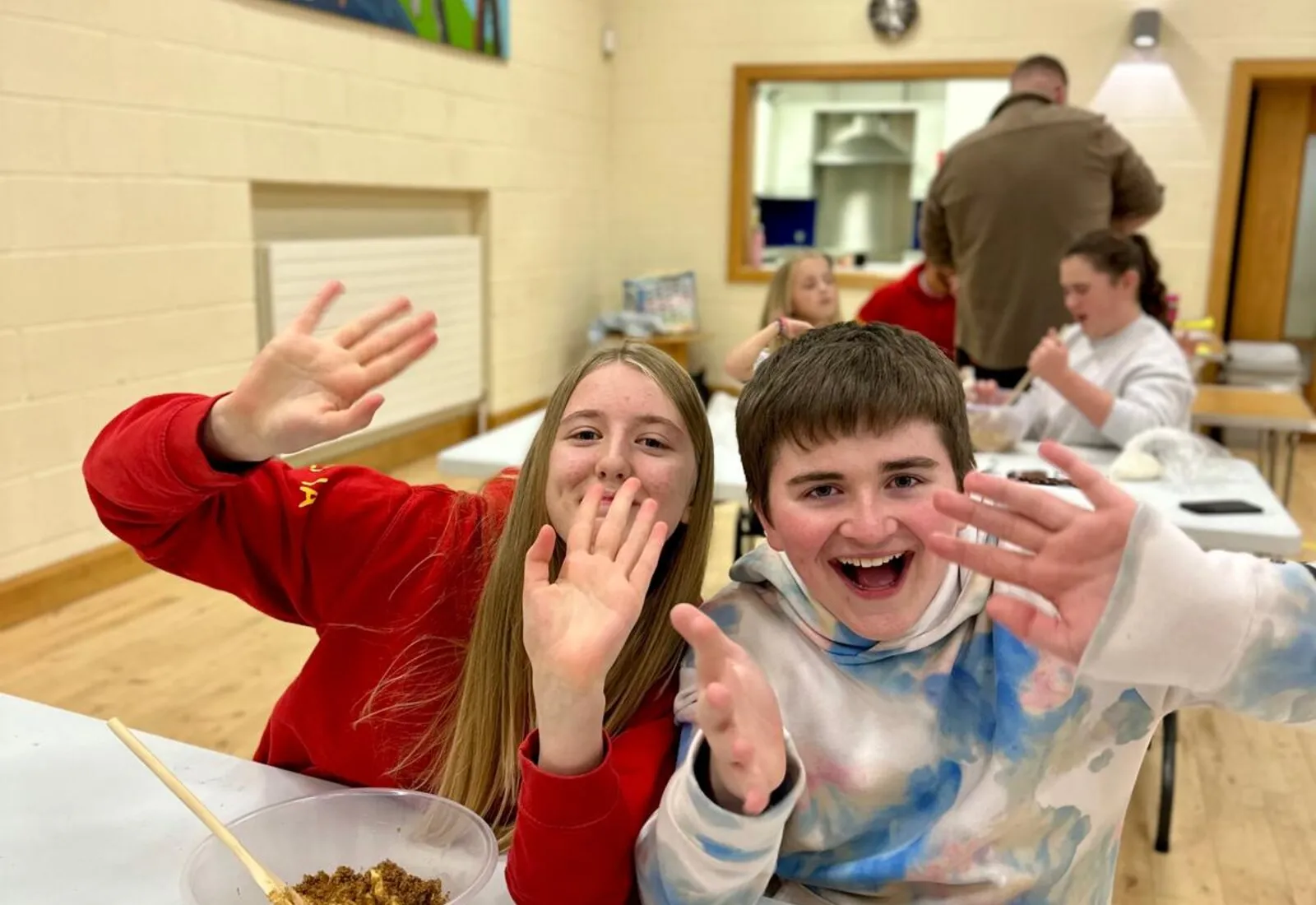 Young people smiling and waving during a youth gathering.